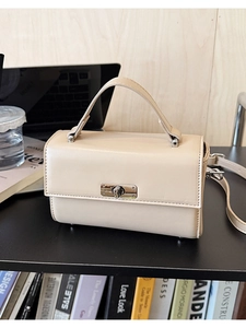 Détail d'un sac bandoulière en cuir beige avec fermoir argenté sur un bureau