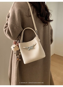 Close-up of litchi texture cream bucket bag with metal lock and plush charm on model