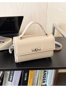 Détail d'un sac à main beige minimaliste avec fermoir rotatif argenté et poignée rigide