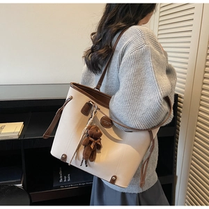 Detail of a beige tote bag with brown leather handles and a cute brown teddy bear charm