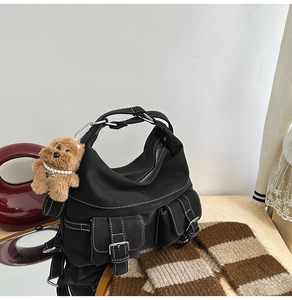 Detail of black utility shoulder bag with white contrast stitching and plush dog charm