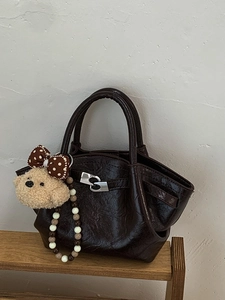 Minimalist deep brown bucket bag with glossy finish and cute plush bear keychain charm