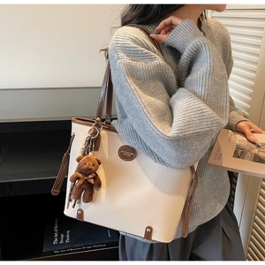 Detail of cream tote bag with brown trim, vintage logo plate and plush bear charm