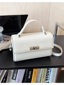 Détail du sac bandoulière blanc cassé avec fermoir rotatif argenté sur une étagère