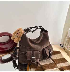 Detail of dark brown hobo bag with plush charm and side pockets on wooden surface