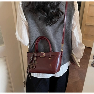 Model showing a vintage wine red crossbody bag with golden hardware and woven charm