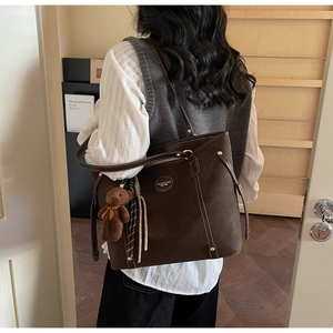 Detail view of large dark brown tote bag featuring white contrast stitching and bear charm