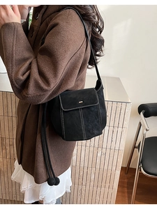 Detail of black suede shoulder bag with white contrast stitching and gold metal buckle