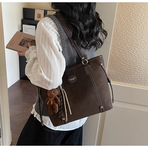 Detail of a dark brown tote bag with white stitching and a cute bear bag charm accessory