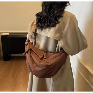 Detail of tan crescent crossbody bag featuring a woven rope knot zipper and durable nylon texture