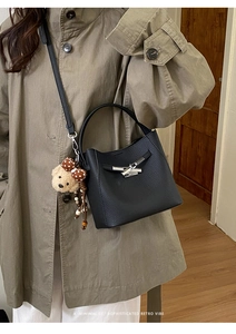 Detail of black lychee grain leather bucket bag with silver clasp and cute bear charm