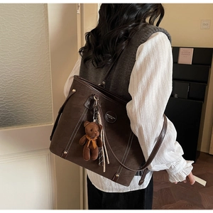 Detail of dark brown tote bag with white stitching, plush bear charm, and gold rivets