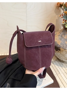 Detail of dark purple leather shoulder bag with white contrast stitching and round charm