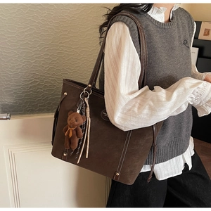 Detail of dark brown tote bag with white stitching and cute plush bear accessory