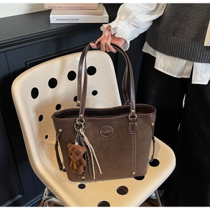 Close-up of dark brown faux leather tote bag with plush bear and fringe accessories