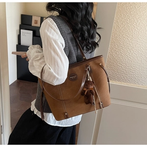 Brown suede tote bag detail with leather strap and plush bear charm on model
