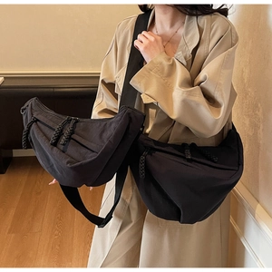 Close-up of black crescent crossbody bag with thick knotted zipper pulls on a beige coat