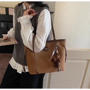 Detail of brown suede tote bag with leather straps and a cute plush bear charm