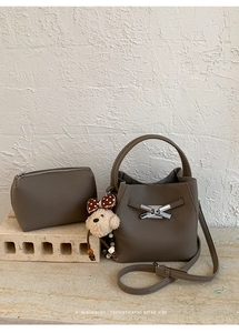 Detail of lychee textured taupe bucket bag with silver bow buckle and puppy charm accessory