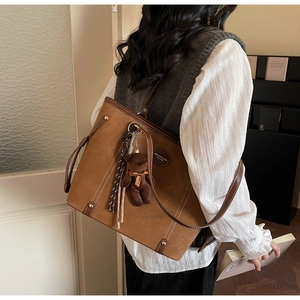 Detailed back view of a caramel suede tote bag with a plush bear charm on a model