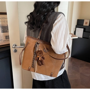 Detail of vintage brown tote bag featuring plush bear charm and suede texture side view