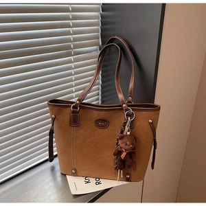 Macro detail of brown suede tote bag with contrast stitching and teddy bear charm