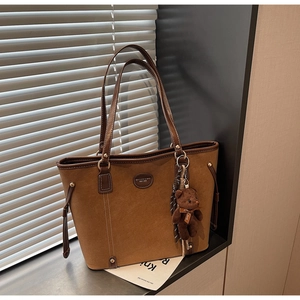 Detail of a brown suede tote bag featuring a leather strap and a plush bear pendant