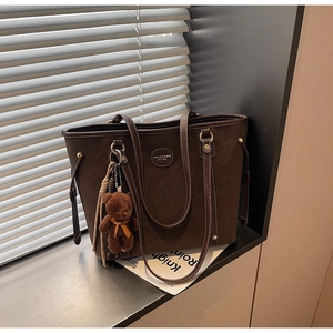 Macro shot of brown tote bag with white stitching and plush bear charm by a window