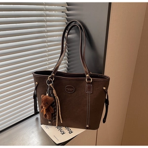 Detail of dark brown tote bag featuring contrast stitching and a plush bear pendant