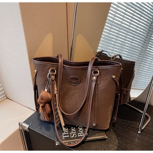 Macro detail of dark brown leather tote with rivet drawstring and plush bear charm