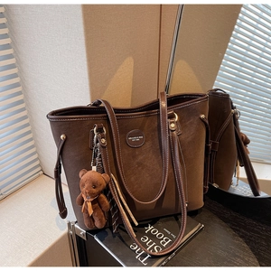 Close-up of dark brown suede tote bag with contrast stitching and bear charm