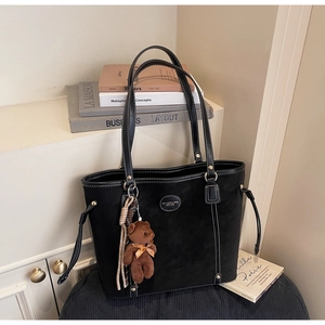Detail of black suede tote bag featuring white stitching and a plush bear charm