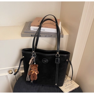 Detail of black tote bag with white stitching, plush bear charm and striped scarf