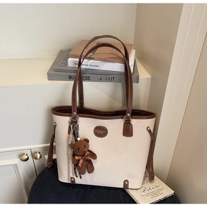 Close-up of beige and brown tote bag with a cute plush bear charm and long shoulder straps