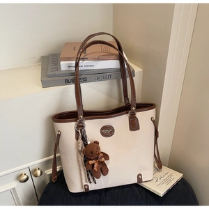 Detail view of a two-tone tote bag with a brown teddy bear charm on a black seat