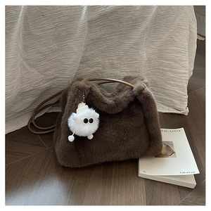Vista dettagliata di una borsa a secchiello in peluche marrone con trama morbida e ciondolo