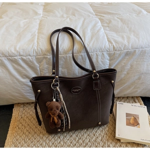 Detail of dark brown tote bag featuring white contrast stitching and plush bear charm