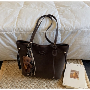 Detail of dark brown leather tote bag with white stitching and cute bear charm