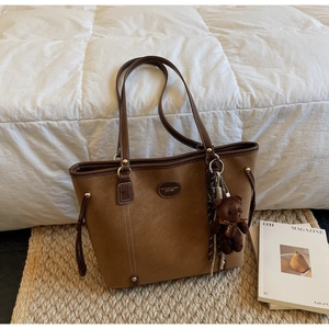 Detail of a brown suede tote bag featuring a plush bear charm and sleek leather straps