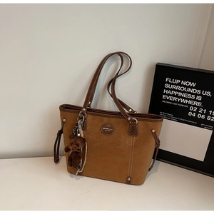 Detail of a brown suede tote bag featuring a leather logo patch and a plush bear charm