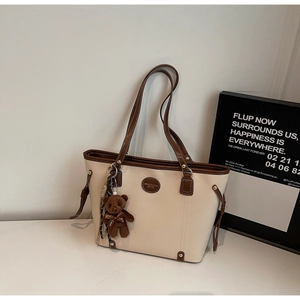 Detail of beige tote bag featuring brown leather trim, side drawstrings and a bear charm