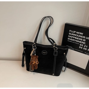 Detail of black tote bag featuring white contrast stitching and a cute plush bear charm