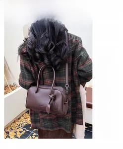 Dettaglio borsa a bauletto in pelle marrone scuro con doppi manici e tracolla sottile