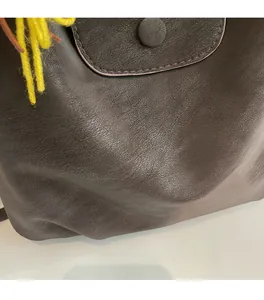Detail of dark brown leather tote featuring a magnetic snap closure and yellow tassel detail
