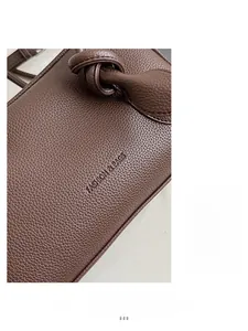 Nahaufnahme von tiefbraunem Leder mit Lychee-Muster, Knotendetail und Logo-Prägung