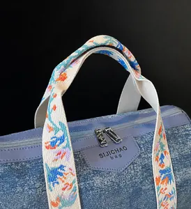Close-up of blue denim tote bag with floral pattern straps and metal dual zippers