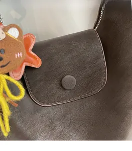Close-up of deep brown pebbled leather bag featuring a flap closure and star bear charm