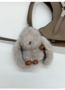 Detail shot of a grey plush rabbit charm with leather accents on a brown handbag