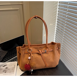 Detail of a brown suede tote bag with metal buckles and a stylish decorative charm