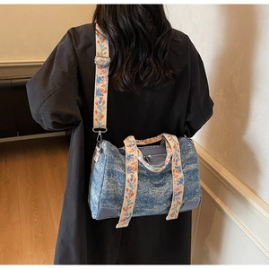 Detail of blue denim Boston bag featuring exquisite floral embroidery on the wide canvas strap
